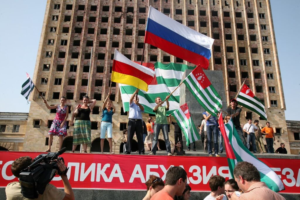 Residents of Sukhumi, the de facto capital of Abkhazia, wave the flags of Abkhazia, South Ossetia, and Russia in celebration of the recognition of their independence by Russia on August 26, 2008, shortly after the Russo-Georgian War. The ruined building behind them once housed the parliament of Abkhazia; it was destroyed during a previous war in the 1990s between Abkhaz separatists and Georgian government forces. Photo: ANP / AFP PHOTO / STR
