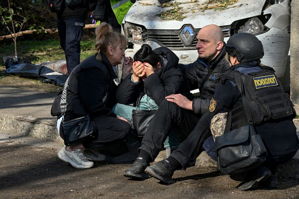 Aangedane bewoners zitten buiten nadat appartementsgebouw in Charkiv is getroffen door een Russische luchtaanval op 13 oktober 2026. De persoon uiterst rechts is een psycholoog die eerste hulp biedt. Foto: Sergey Bobok / ANP / AFP
