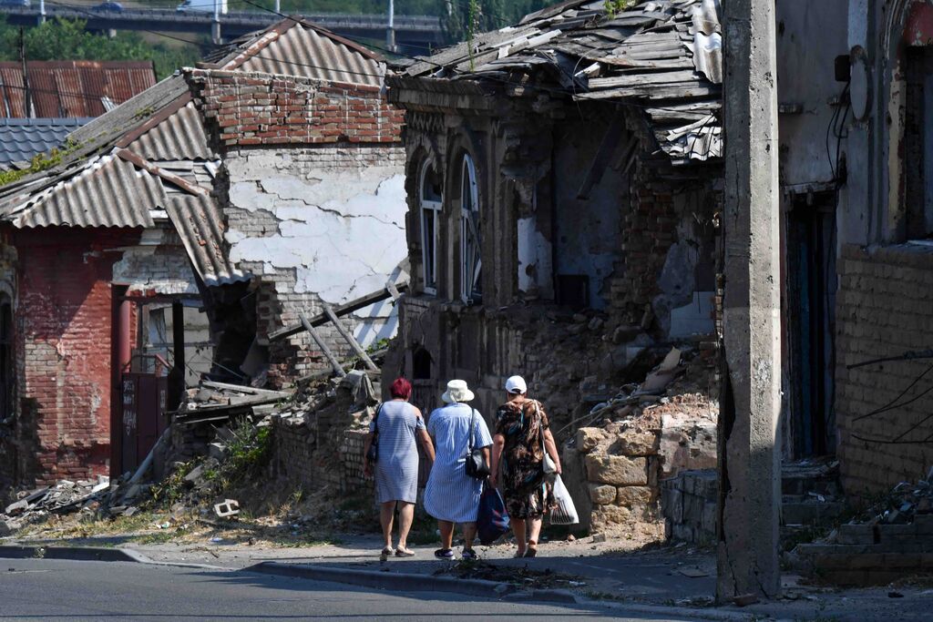 Vrouwen lopen langs verwoeste huizen in de door Rusland bezette Oekraïense stad Marioepol, in 2025. Foto: ANP / Olga Maltseva / AFP